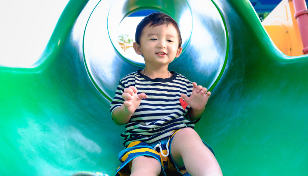 Little Asian Kid Playing Slide At The Playground