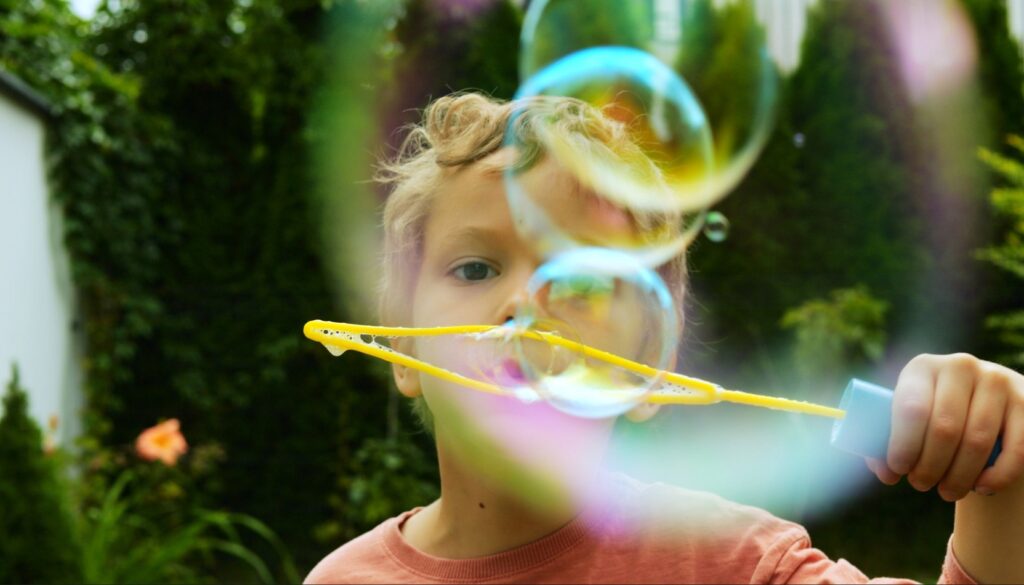Curly-haired,Toddler,Boy,Releases,Even,Row,Of,Soap,Bubbles,From