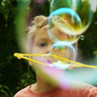Curly-haired,Toddler,Boy,Releases,Even,Row,Of,Soap,Bubbles,From